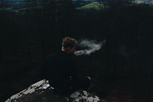 Sigara içen bir kayaya oturan