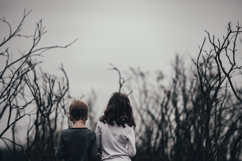 Băiat şi fată în picioare printre copaci
