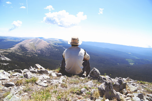 Kille med hatt sitter på en bergstopp