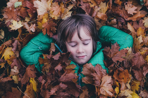 Băiat sub o patura de frunze