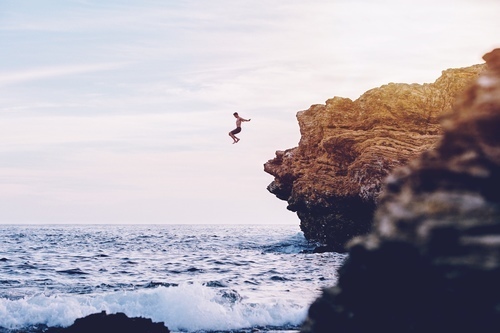 Человек прыгает в воду из скалы